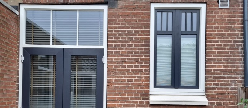 Kunststof: dé keuze voor deuren en kozijnen. Donkerblauwe kozijnen in een bakstenen muur.