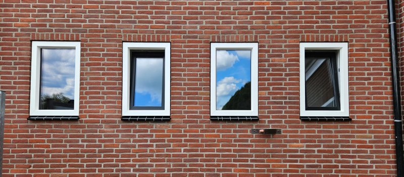 Vier kunststof kozijnen ramen in een bakstenen muur.