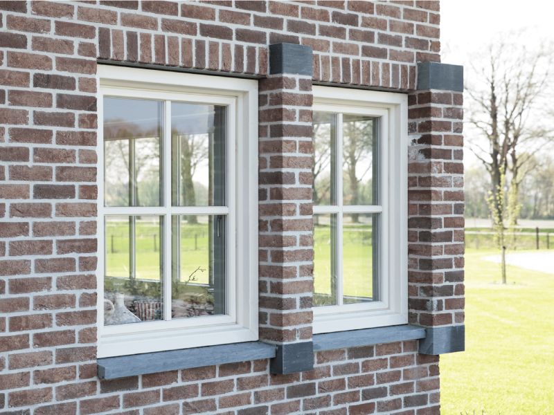 Bakstenen gevel van woning in landelijke omgeving voorzien van kunststof kozijnen.